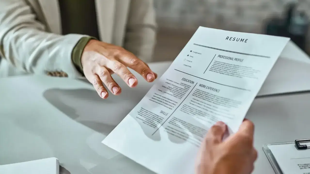 Mani che si passano un curriculum vitae. Un candidato presenta il suo cv, mostrando cosa scrivere per fare una buona impressione.