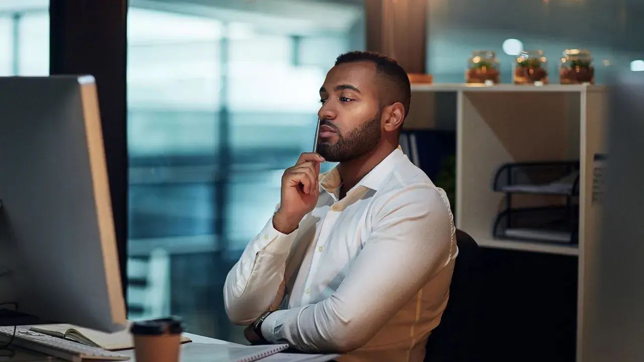 Uomo d'affari pensa al suo curriculum vitae, esperienze lavorative, con una penna tra le labbra, davanti al computer.