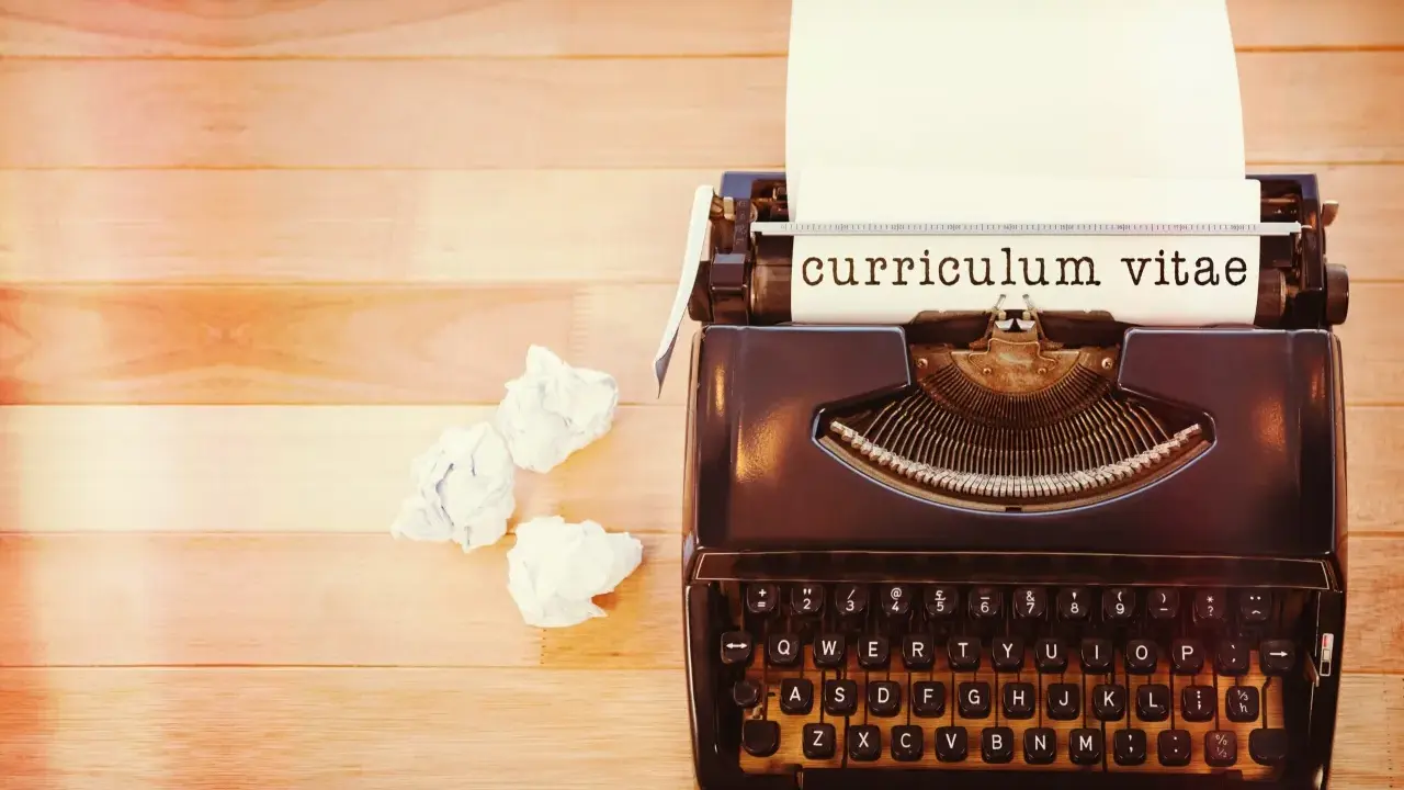 Macchina da scrivere con foglio su cui è scritto "curriculum vitae". Accanto, fogli accartocciati, simbolo di un cv cronologico in lavorazione.