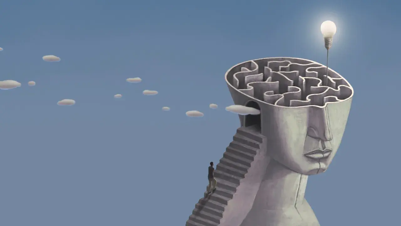 Un uomo sale una scala verso un labirinto nella testa di una statua, simbolo di esempi di problem solving nella vita quotidiana. Una lampadina illumina la soluzione.