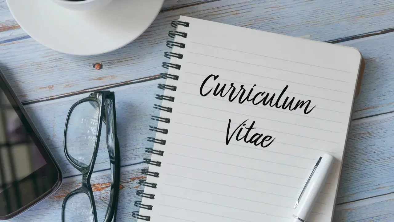 Taccuino con scritto "Curriculum Vitae", occhiali, smartphone e tazza di caffè. Preparazione per il curriculum trattamento dati.