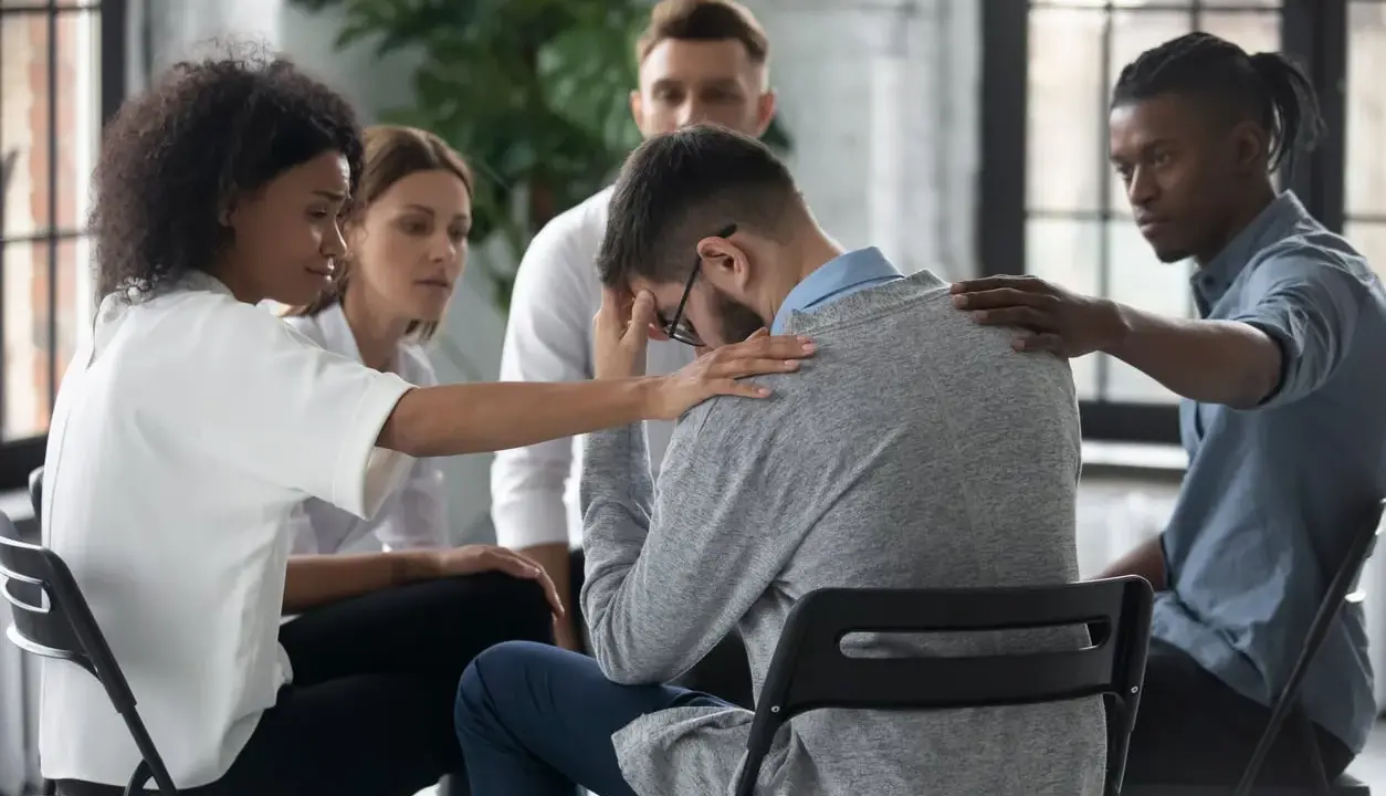 Un gruppo di persone offre supporto a un uomo visibilmente turbato, mostrando la curva del cambiamento attraverso l'empatia e la solidarietà.