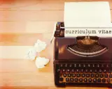 Macchina da scrivere con foglio su cui è scritto "curriculum vitae". Accanto, fogli accartocciati, simbolo di un cv cronologico in lavorazione.