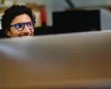 Uomo con occhiali blu sorride guardando il monitor, pensando a come migliorare le sue competenze digitali per il CV.