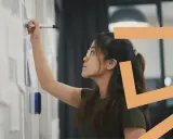Donna con occhiali scrive su una lavagna. Il titolare di una ditta individuale può essere assunto come dipendente, esplorando nuove opportunità.