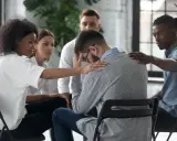 Un gruppo di persone offre supporto a un uomo visibilmente turbato, mostrando la curva del cambiamento attraverso l'empatia e la solidarietà.