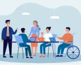Team di lavoro eterogeneo, con persone di diverse età e un uomo in carrozzina, che collaborano in un ufficio moderno. Esempio di diversity management.