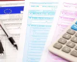 Documenti fiscali per il commercio auto usate regime forfettario. Penna e calcolatrice su moduli IVA.
