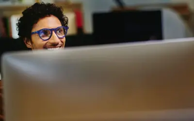 Uomo con occhiali blu sorride guardando il monitor, pensando a come migliorare le sue competenze digitali per il CV.