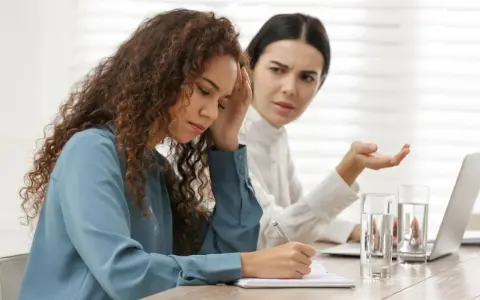Due donne in ufficio, una con la mano sulla fronte, l'altra gesticola. Difficile gestione dei conflitti sul lavoro.