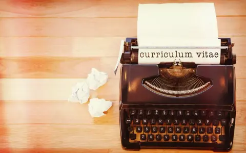 Macchina da scrivere con foglio su cui è scritto "curriculum vitae". Accanto, fogli accartocciati, simbolo di un cv cronologico in lavorazione.