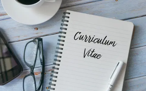 Taccuino con scritto "Curriculum Vitae", occhiali, smartphone e tazza di caffè. Preparazione per il curriculum trattamento dati.