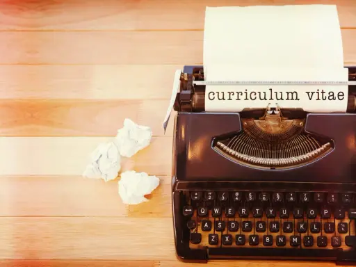 Macchina da scrivere con foglio su cui è scritto "curriculum vitae". Accanto, fogli accartocciati, simbolo di un cv cronologico in lavorazione.