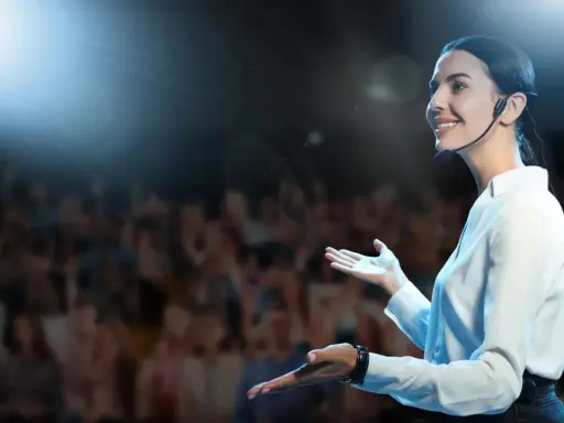 Donna sorridente con microfono, sul palco davanti a un pubblico. Esercizi per parlare in pubblico efficaci.