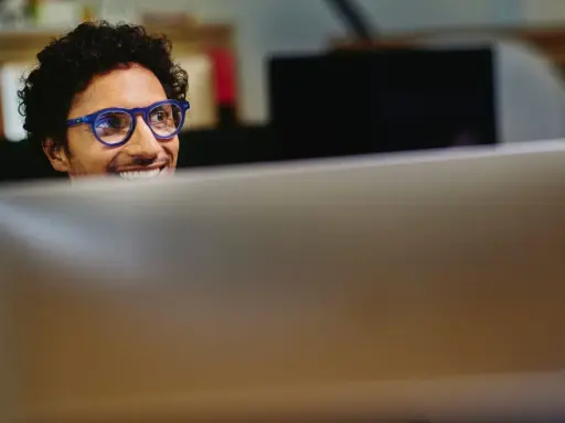 Uomo con occhiali blu sorride guardando il monitor, pensando a come migliorare le sue competenze digitali per il CV.