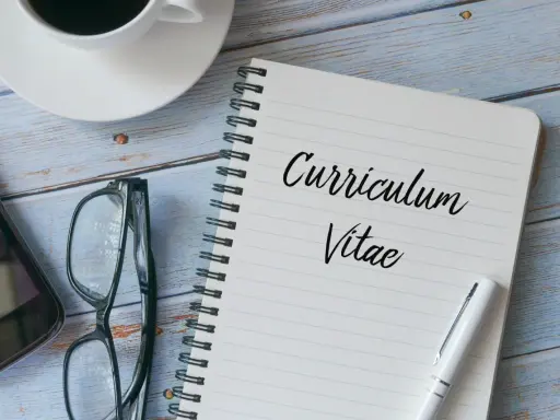 Taccuino con scritto "Curriculum Vitae", occhiali, smartphone e tazza di caffè. Preparazione per il curriculum trattamento dati.