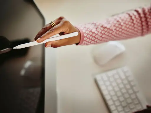 Mano con stilo bianco che interagisce con uno schermo, mentre sullo sfondo si intravedono tastiera e mouse. Ottimizzazione del cv per i sistemi ats.