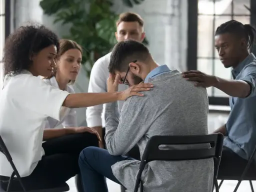 Un gruppo di persone offre supporto a un uomo visibilmente turbato, mostrando la curva del cambiamento attraverso l'empatia e la solidarietà.