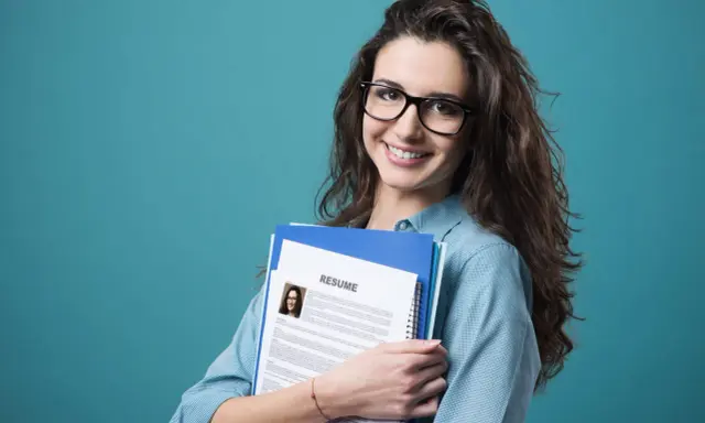 Young woman with glasses holding a resume and folders against a teal background.