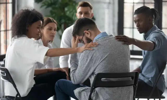 Un gruppo di persone offre supporto a un uomo visibilmente turbato, mostrando la curva del cambiamento attraverso l'empatia e la solidarietà.