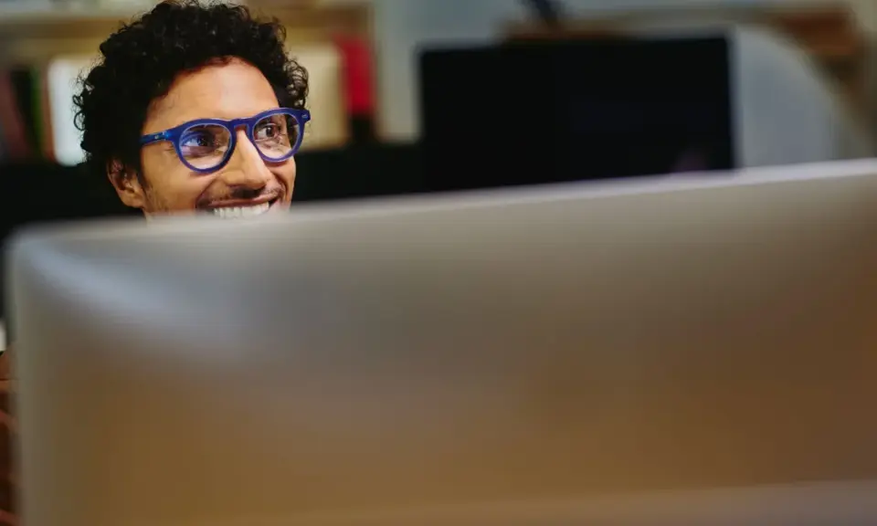Uomo con occhiali blu sorride guardando il monitor, pensando a come migliorare le sue competenze digitali per il CV.