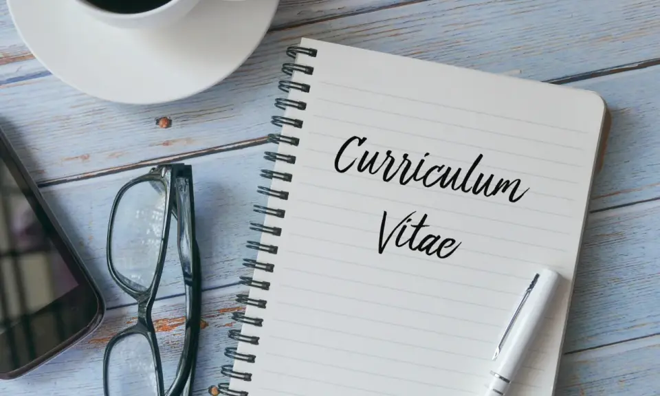 Taccuino con scritto "Curriculum Vitae", occhiali, smartphone e tazza di caffè. Preparazione per il curriculum trattamento dati.
