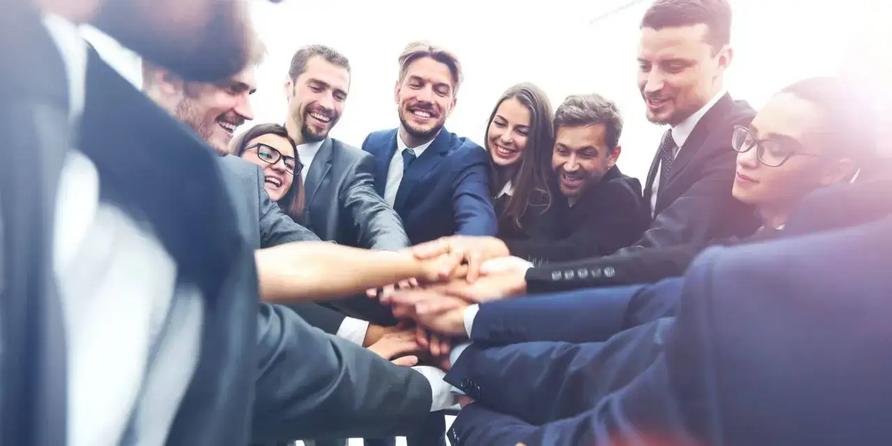Un gruppo di professionisti sorridenti unisce le mani, dimostrando la loro capacit&agrave; di leadership e spirito di squadra.
