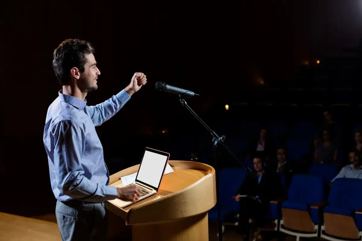 Uomo sul palco, con pugno alzato, che tiene una lezione. Esercizi per parlare in pubblico.