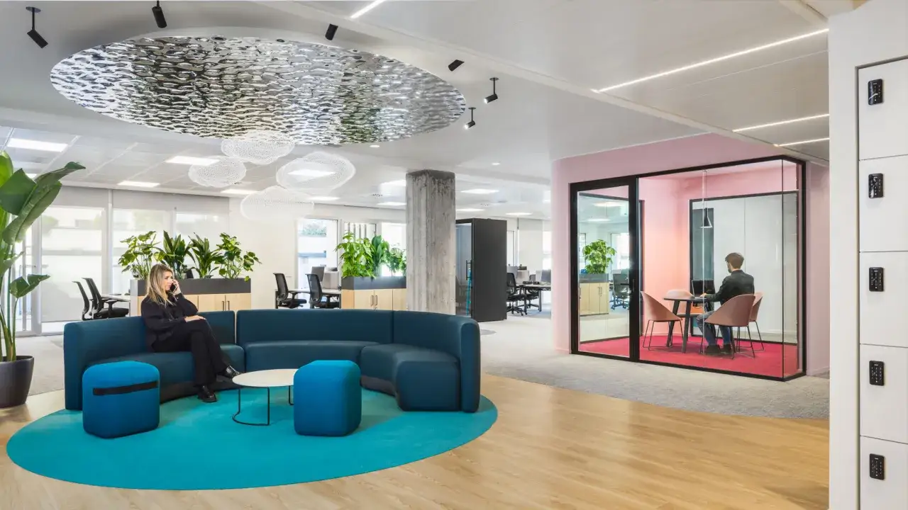 Interni moderni con divano blu, piante e una sala riunioni in vetro. Un interior designer con partita iva potrebbe creare spazi cos&igrave;.