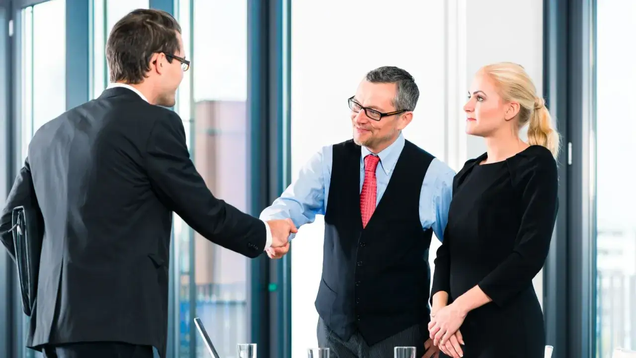 Un uomo d'affari stringe la mano a un hiring manager sorridente, mentre una donna in nero osserva.