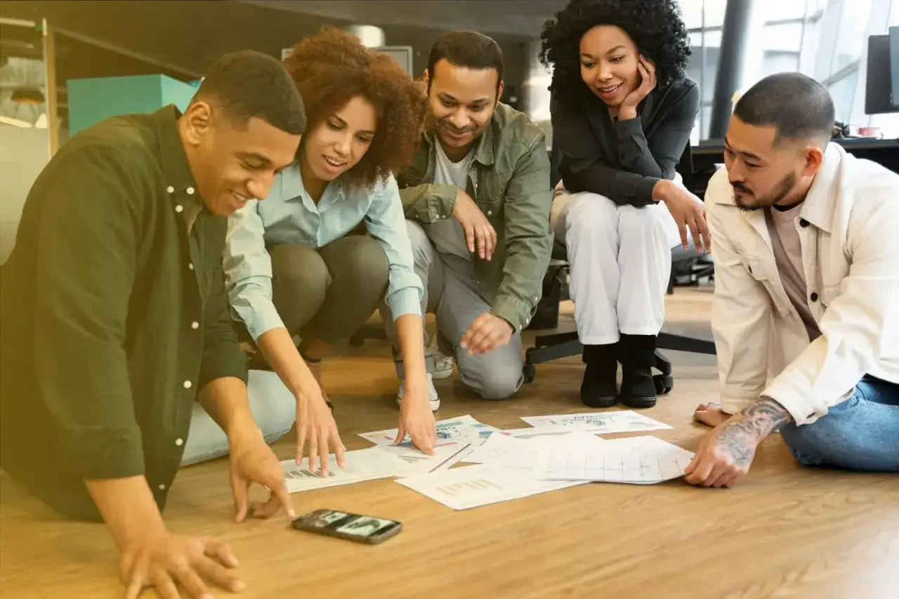 Un gruppo di persone discute idee su fogli sparsi, mostrando cos'&egrave; il pensiero laterale: un approccio creativo e non convenzionale alla risoluzione dei problemi.