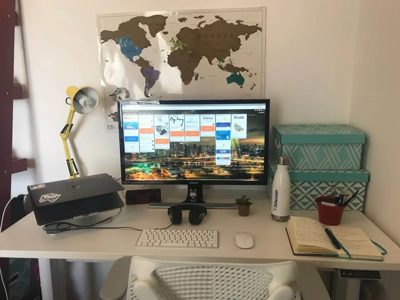 Postazione di lavoro per il remote working: monitor con dashboard, laptop, mappa del mondo e lampada gialla.