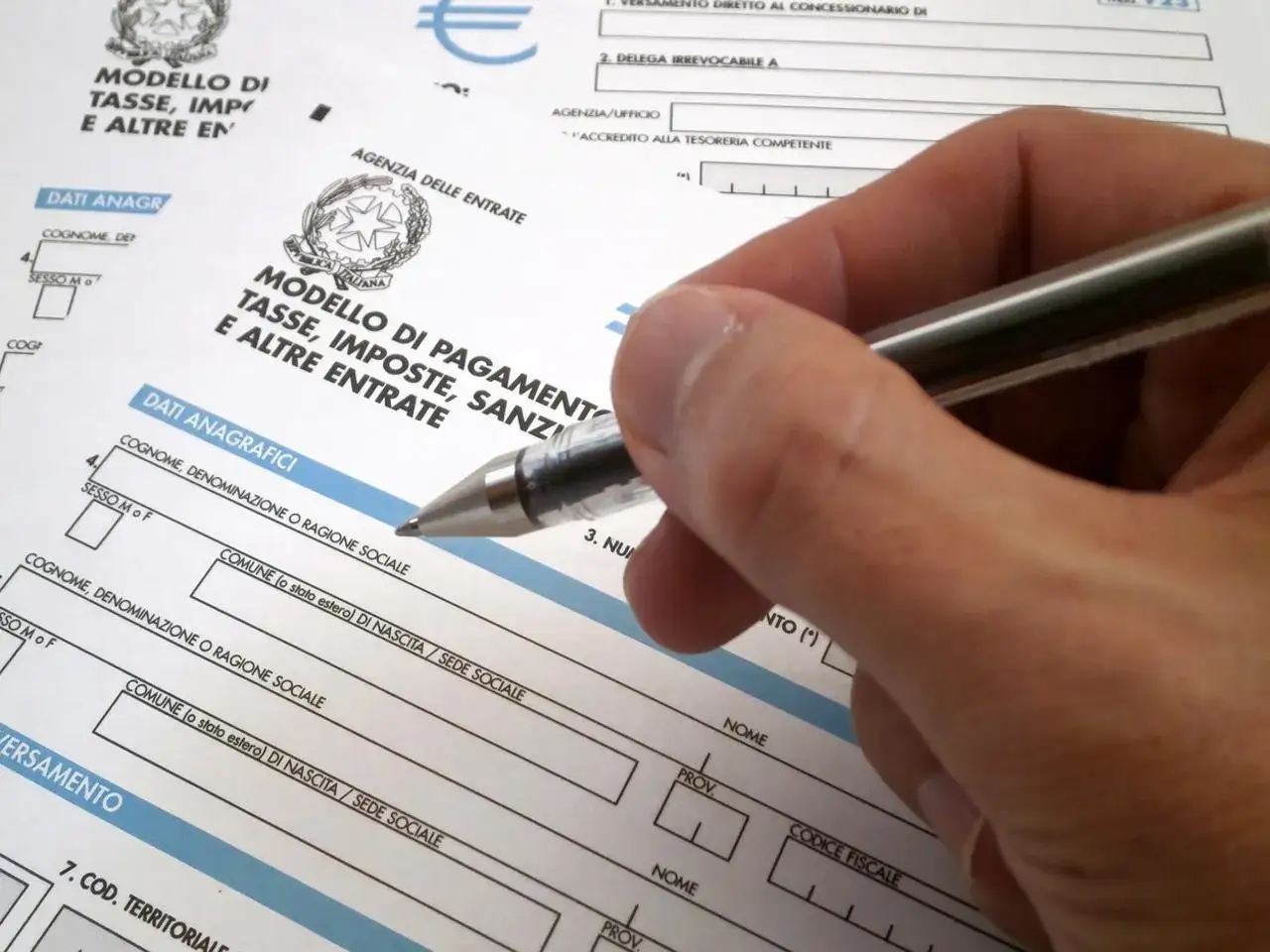 Hand holding a pen over Italian tax forms.