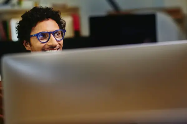 Uomo con occhiali blu sorride guardando il monitor, pensando a come migliorare le sue competenze digitali per il CV.