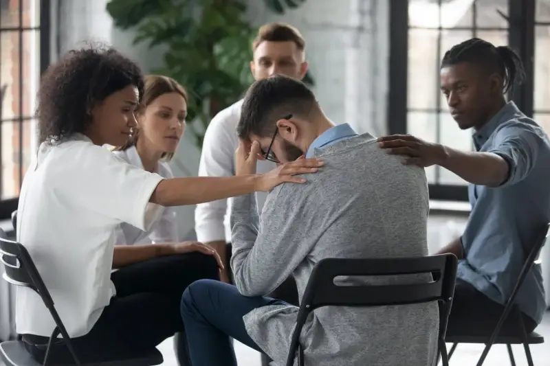 Un gruppo di persone offre supporto a un uomo visibilmente turbato, mostrando la curva del cambiamento attraverso l'empatia e la solidarietà.